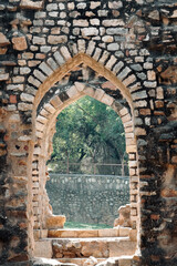 Old brick wall with arched entrance. Remains of ancient architecture at the complex of Qutb Minar tower in Delhi, India.