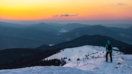 backpacker girl admires the scenery while standing on top of a mountain snowy ridge, colorful winter sunset seen from the top of the bukowe berdo mountain