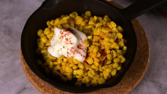 Esquites, grilled corn, served with sour cream and sprinkled with chili powder in cast iron pan. Mexican street food meal