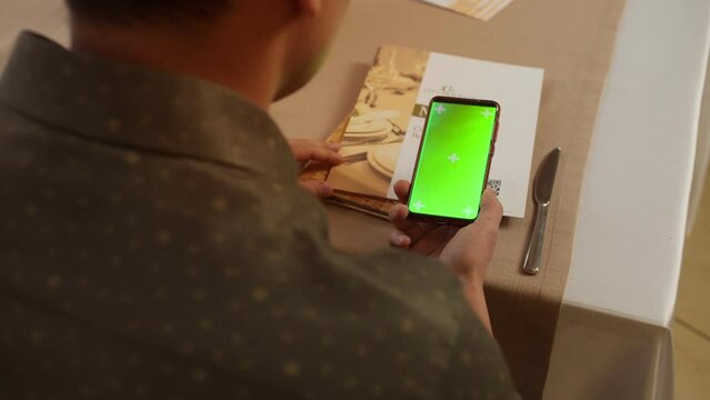 Caucasian man scanning qr code with smartphone with chroma green screen top view, online menu in cafe or scanning QR code in restaurant