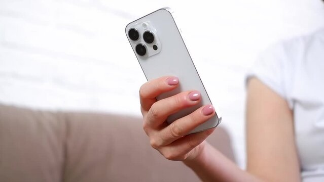 Woman hand is holding and touching iphone 14 and looking at the screen of mobile phone in light room.