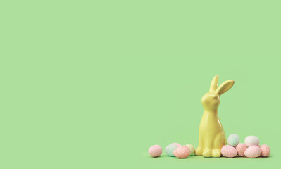 Yellow Easter bunny with many tiny eggs sweets around on green edgeless background. Happy Easter holiday concept. Easter chocolate treats web banner