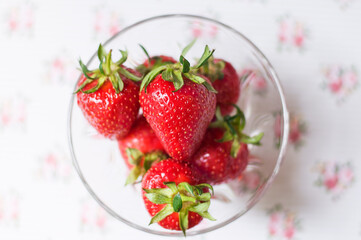 Strawberries in a glass bowl on a light background with roses. View from above
