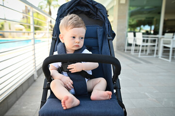 Sweet baby boy sitting in a stroller outdoors. Little child in pram.