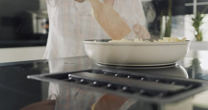 Senior woman fries potatoes on an induction electric stove with a built-in extractor fan