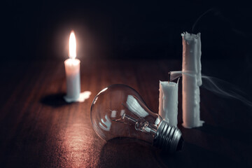 Blackout. Lights out, unlit bulb next to a burning candle in complete darkness. Darkened city,...