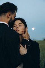 young stylish couple of husband and wife dressed in classic suits on a photo shoot in the middle of a green field. The concept of the relationship between a couple of people in love