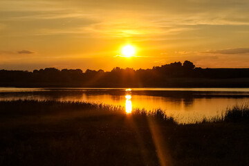 Beautiful, golden sunset sunrise over a lake. Crepuscular rays and clouds reflected in calm water