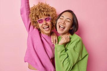 Horizontal shot of two women express positivity and joy laugh happily and exclaim loudly stand...