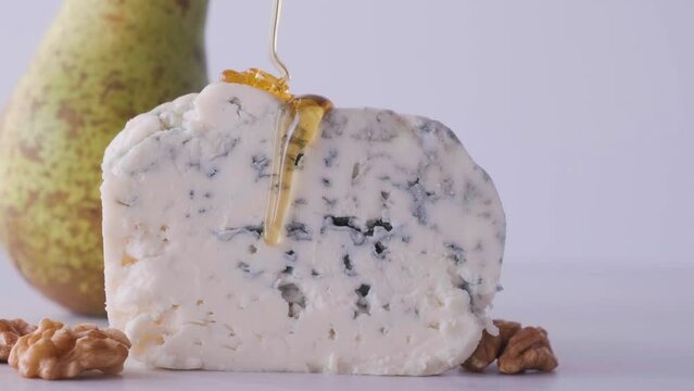 Pouring honey on blue cheese dorblu or gorgonzola with pear and walnuts on white background. Close up. Tasty food