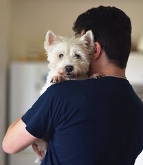 a man holds a white dog in his arms