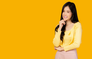 Happy Thinking young asian woman standing isolated over yellow background Look aside to copy space with happiness and smile face Pretty girl keeps finger on chin being deep in thought Good thinking