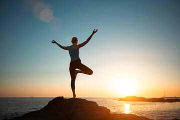 A woman doing yoga, meditating on the ocean shore, seeing off the sun.