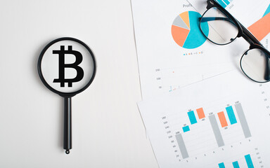 Investment in blockchain financial business concept. Magnifier focused on bitcoin cryptocurrency sign, economic documents with analytical infographics, charts and graphs