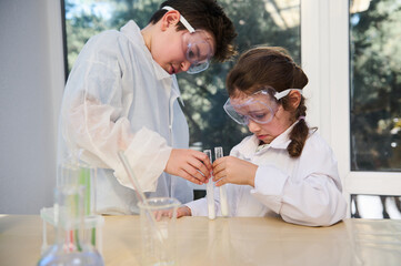 Concentrated Caucasian smart kids conducting chemical experiment, watching the reaction taking...