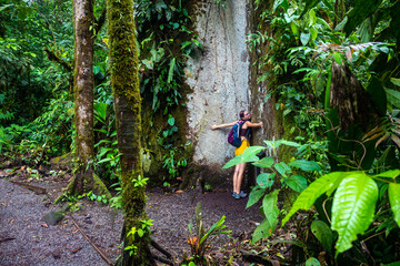 Backpacker girl hugs huge tree in Costa Rican rainforest; love of nature, closeness to nature and appreciation of vegetation
