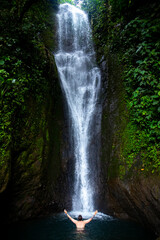 man spreads his arm standing under hidden tropical waterfall in costa rica; waterfall in the rainforest; don jose waterfalls