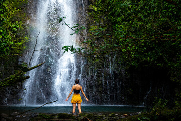 A beautiful girl spreads her arms while standing under a tropical waterfall in Costa Rica; swimming...