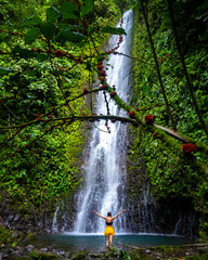 A beautiful girl spreads her arms while standing under a tropical waterfall in Costa Rica; swimming...
