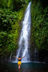 A beautiful girl spreads her arms while standing under a tropical waterfall in Costa Rica; swimming in a hidden waterfall in the rainforest; don jose waterfalls