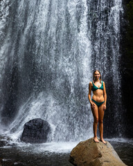 Fototapeta na wymiar beautiful girl in a bikini standing under a tropical waterfall in Costa Rica; swimming in a hidden waterfall in the rainforest
