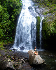 beautiful girl in a bikini sitting under a tropical waterfall in Costa Rica; swimming in a hidden waterfall in the rainforest