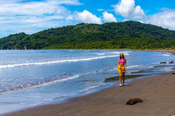 A woman in a shorts walks on a paradise Costa Rican beach with an island in the background admiring the unique views