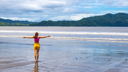 A woman in a shorts walks on a paradise Costa Rican beach with an island in the background admiring the unique views