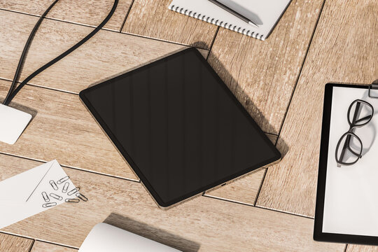 Perspective view on modern digital tablet with blank dark screen and space for your logo or text on wooden parquet surface among office tools. 3D rendering, mock up