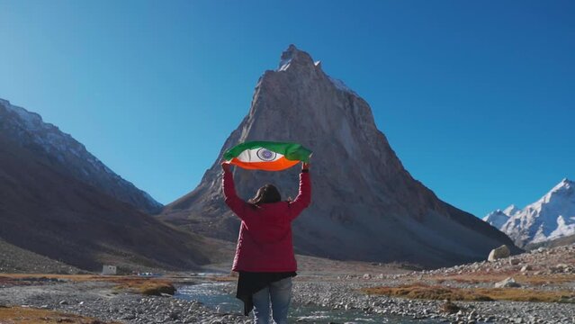 Wide angle shot of female Indian traveler holding Indian flag above her head in front of Gumbok Rangan mountain at Zanskar, Ladakh, India. Indian flag waving in the wind. Indian flag background