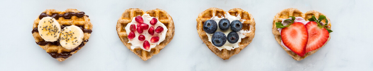 A narrow view of a row of mini heart shaped waffles with various toppings,