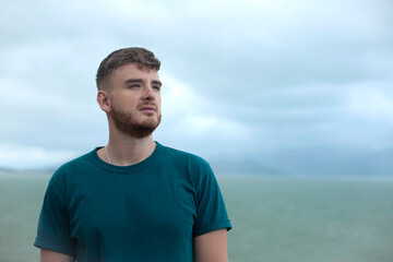 Serious pensive thoughtful handsome happy guy, young man enjoying sea, ocean view, landscape, looking into distance at summer day in tropical country at storm with cloudy sky, breathing deep fresh air