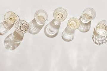 Fototapeta na wymiar Top view white sparkling wine in different glasses of wine, stemmed glass with sun shadow and glare on light beige background. White wine tasting concept flat lay, copy space. Summer drinks