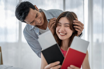 Obraz premium Asian couple surprises girlfriend with plane ticket and passport to hang out together on vacation in their bedroom at home