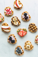 Diagonal rows of mini heart shaped waffles with various toppings.