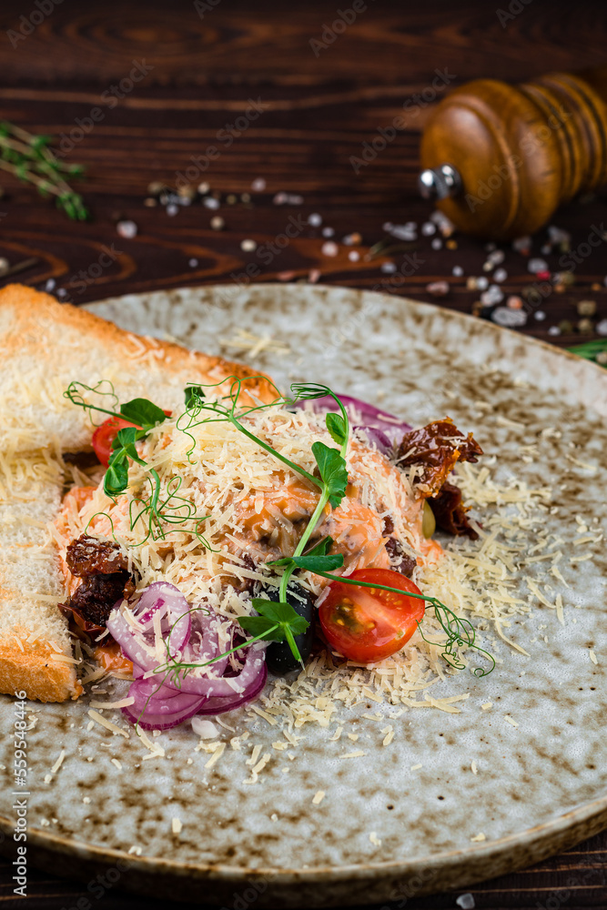 Wall mural lunch red fish with cheese, tomatoes, sun-dried tomatoes, olives, onions, greens and toast in a plat