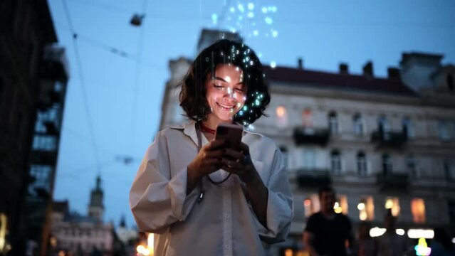 Beautiful Smiling Woman Using Smartphone on a City Street at Night. Wireless communication network concept. Mobile technology. Visualization of Information Lines Flying from Mobile Phone