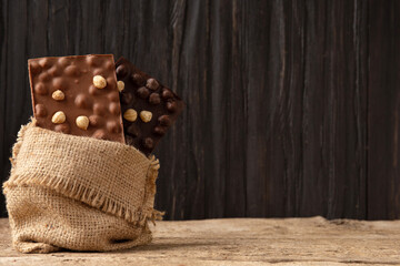 Fototapeta na wymiar Bars of black and milk chocolate with chocolate chips in a bag on an old wooden background