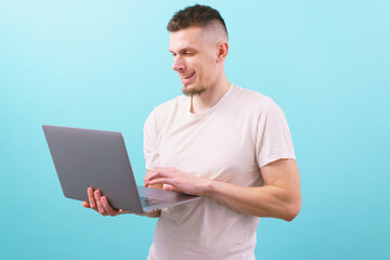 Smart young student smiling and using laptop on a blue background. Smart. Student. Happiness. Worker. Smiling. Caucasian. Alone. Application. Confident. Confidence. Excited. Energetic. Enthusiastic