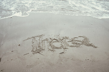 The name Theresa written in the sand as a wave comes closer