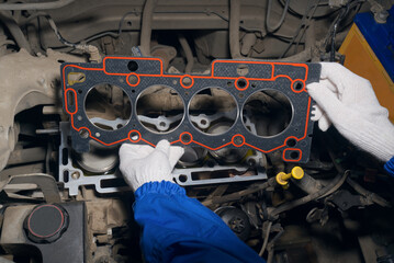 An auto mechanic installs a gasket on a car engine block. Service of diagnostics, repair and...