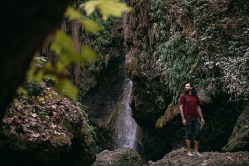 Obraz premium A young male tourist stands near a tropical waterfall among the rocks.