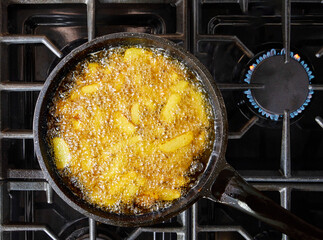 French fries draining the excess fat, after frying, in a sieve. Fries are deep-fried stick potatoes, a traditional side option of the French culinary.