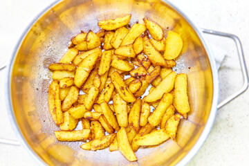 French fries draining the excess fat, after frying, in a sieve. Fries are deep-fried stick potatoes, a traditional side option of the French culinary.