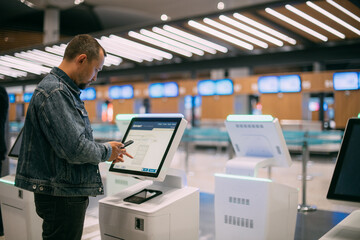 A male passenger at the electronic check-in desk in the departure area of the modern airport terminal.