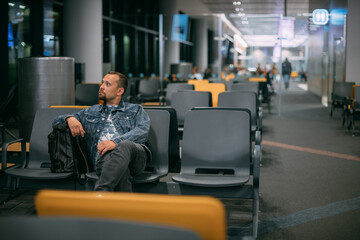 Fototapeta na wymiar A male passenger is sitting waiting for boarding in the departure area of the modern airport terminal.