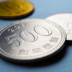 Translation: Bank of Korea. Korean coins lie on blue paper surface. 500 won coin close up. Square illustration about economy, finance or bank. Money and business in South Korea. Macro