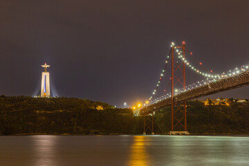 Fototapeta premium Long exposure photo of the 25th of April bridge in Lisbon, Portugal with the Sanctuary of Christ the King to the left