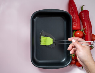 A hand greases a baking dish with oil. Green cooking brush