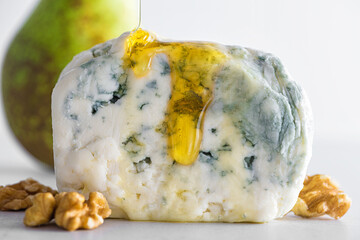 Pouring honey on blue cheese dorblu or gorgonzola with pear and walnuts on white background. Close...